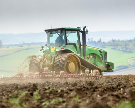 Un agricultor conduce un tractor verde sobre tierra arada